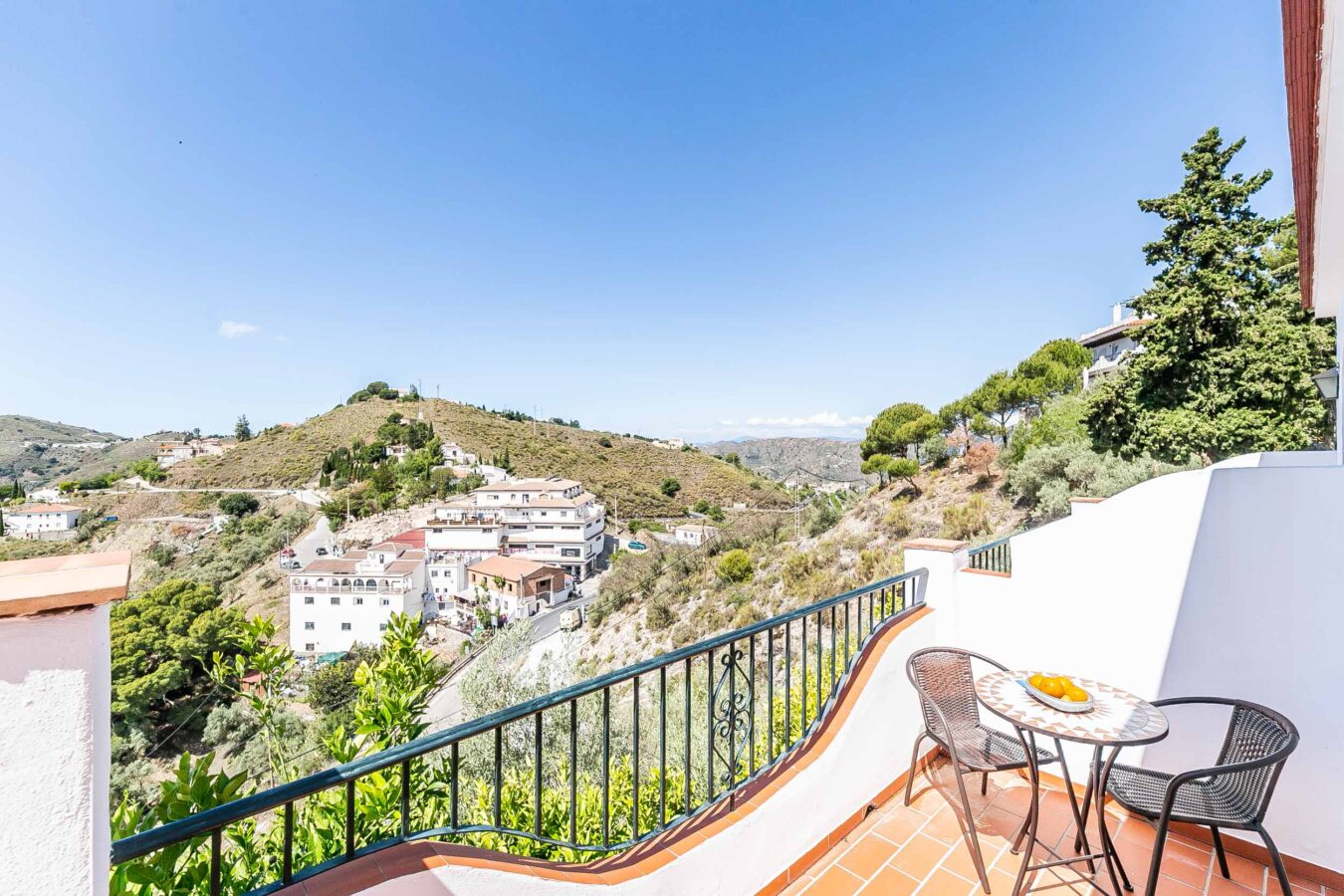 bakker og hvide bygninger.|Solbeskinnet bjergby omgivet af grønne bakker og blå himmel.|Charmerende hvid by placeret på bjergskråning under blå himmel.|Fredeligt hjørne med pool og liggestole i det sydspanske landskab.