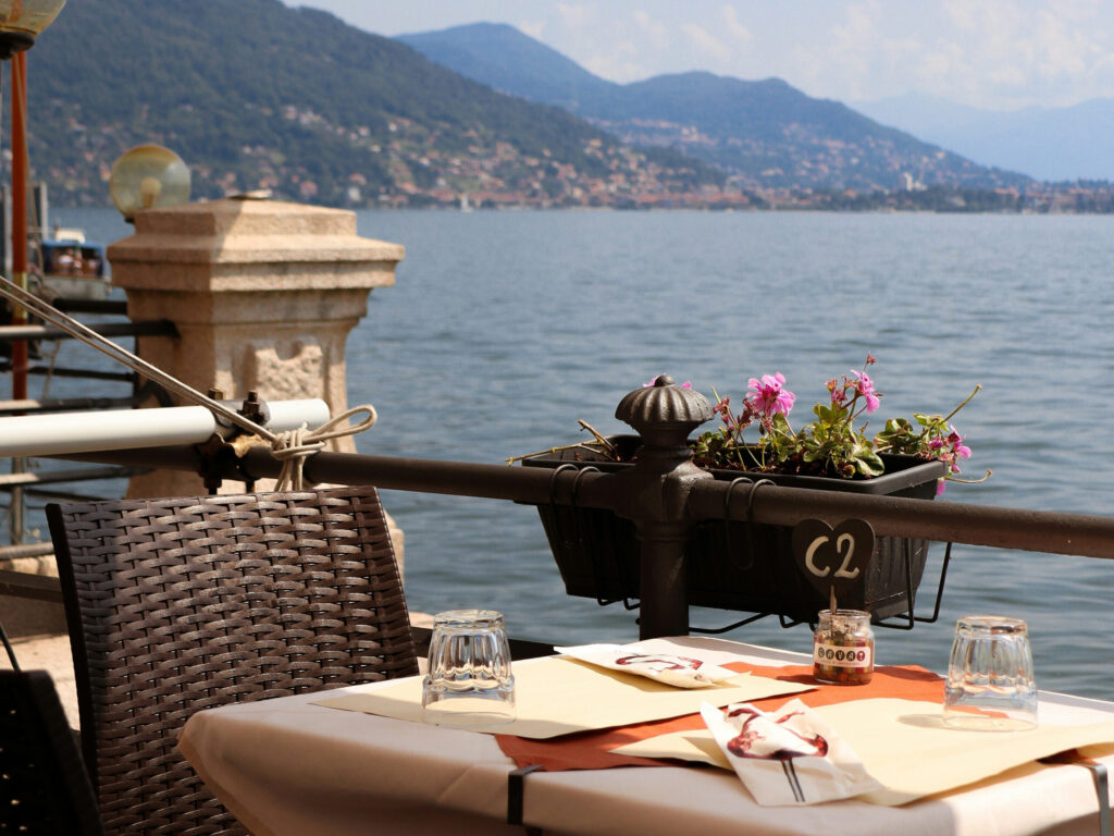 Dækket cafébord med udsigt over Lago Maggiore i Baveno, Italien, omgivet af bjerge og vand.