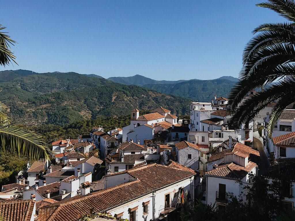 Solbeskinnet bjergby omgivet af grønne bakker og blå himmel.