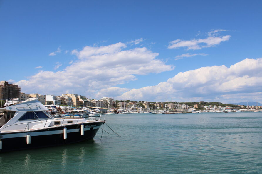 azurblåt vand og byens skyline i baggrunden.|Udsigt over kystbyen ved solnedgang med oplyste gader